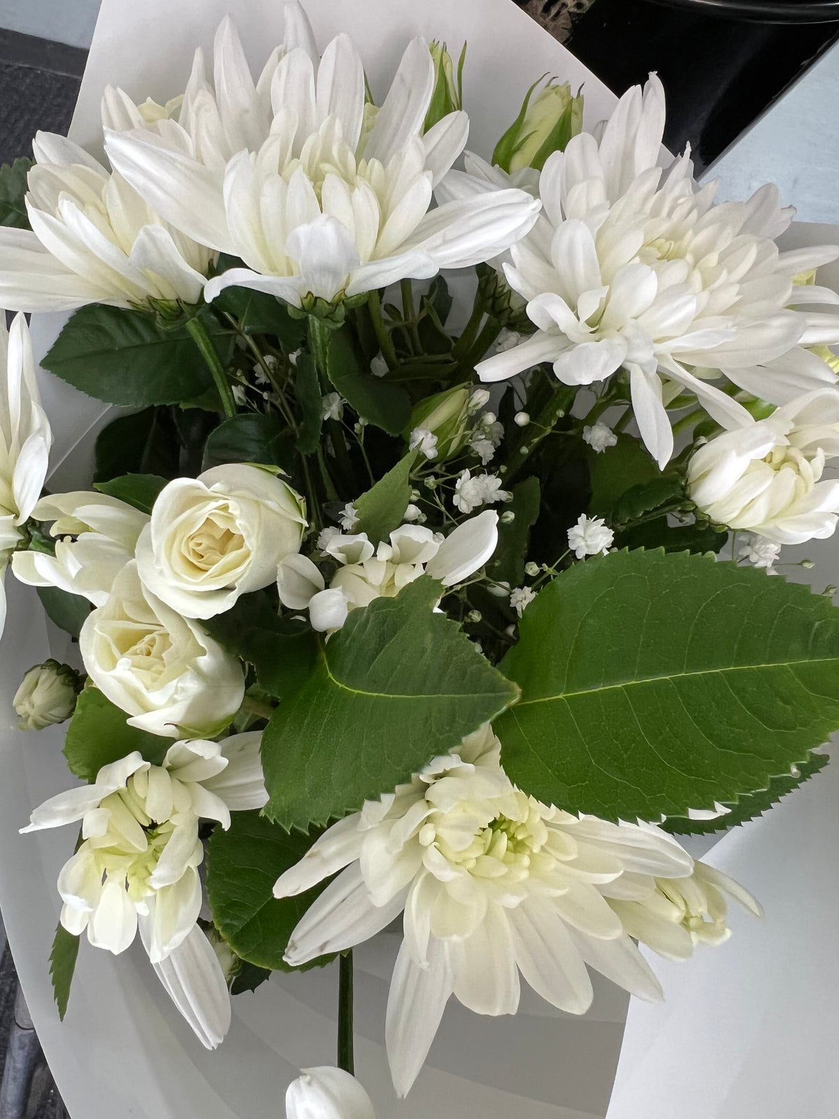 Exceptional White bouquet with layered white blooms, creamy rosebuds and green foliage in white wrapping